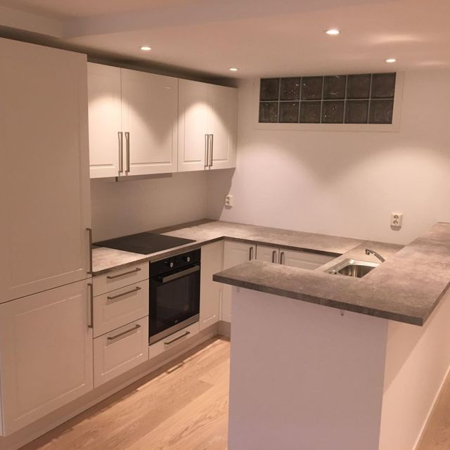 Moderne og lyst kjøkken med en ovn, kjøleskap, vask og spotlys i taket. 